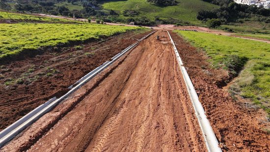 Via do loteamento vista do alto, com guias de concreto já instaladas e a serra ao fundo